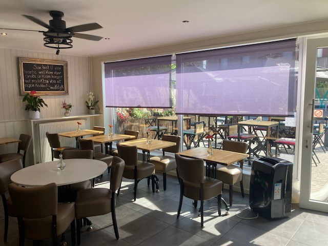 Binnenzicht van broodjeszaak San's Place — houten tafels met verse bloemen in de verbruikszaal in Sint-Job-in-'t-Goor